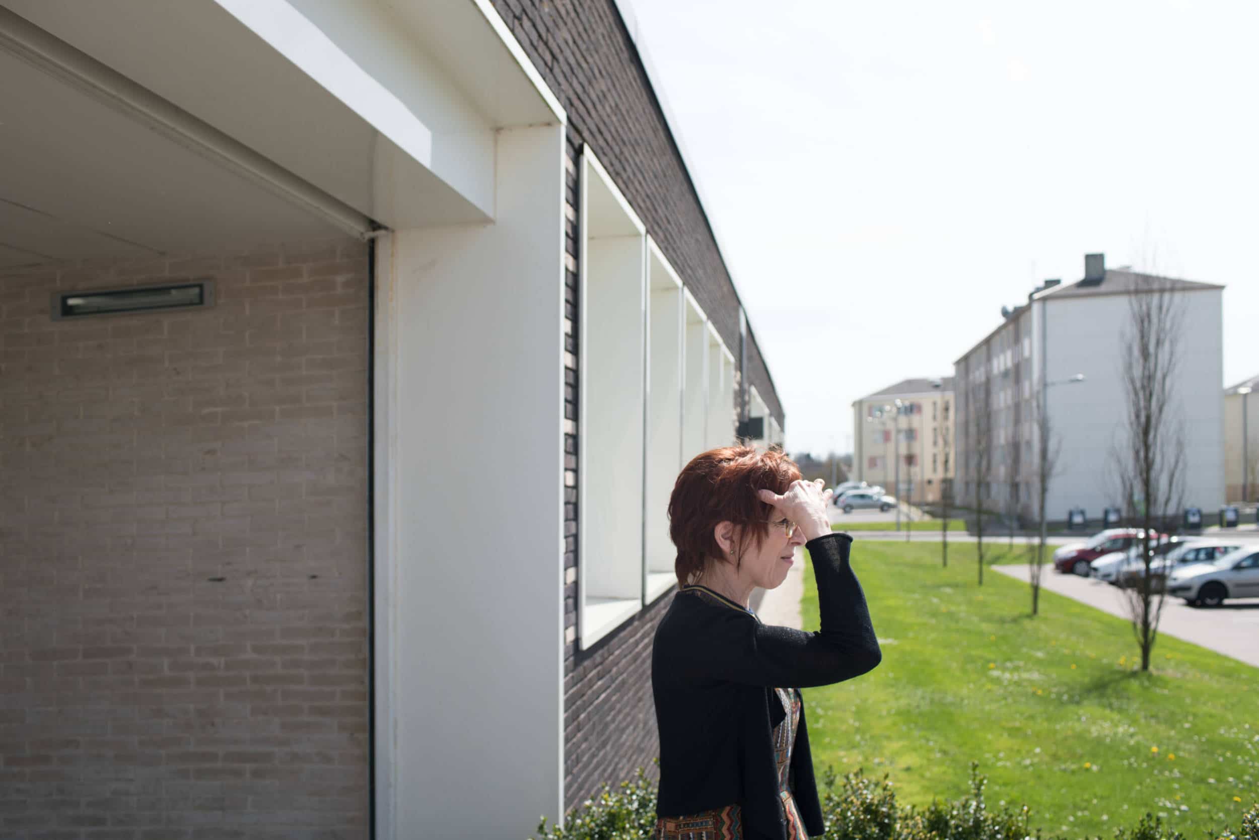 Isabelle, à l'extérieur du bâtiment, regarde au loin en mettant sa main en visière pour se protéger du soleil