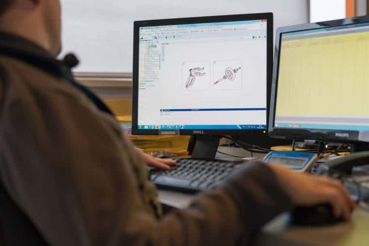 Au premier plan, les mains d'Edouard manipulent souris et clavier d'ordinateur. Les moniteurs sont visibles au second plan
