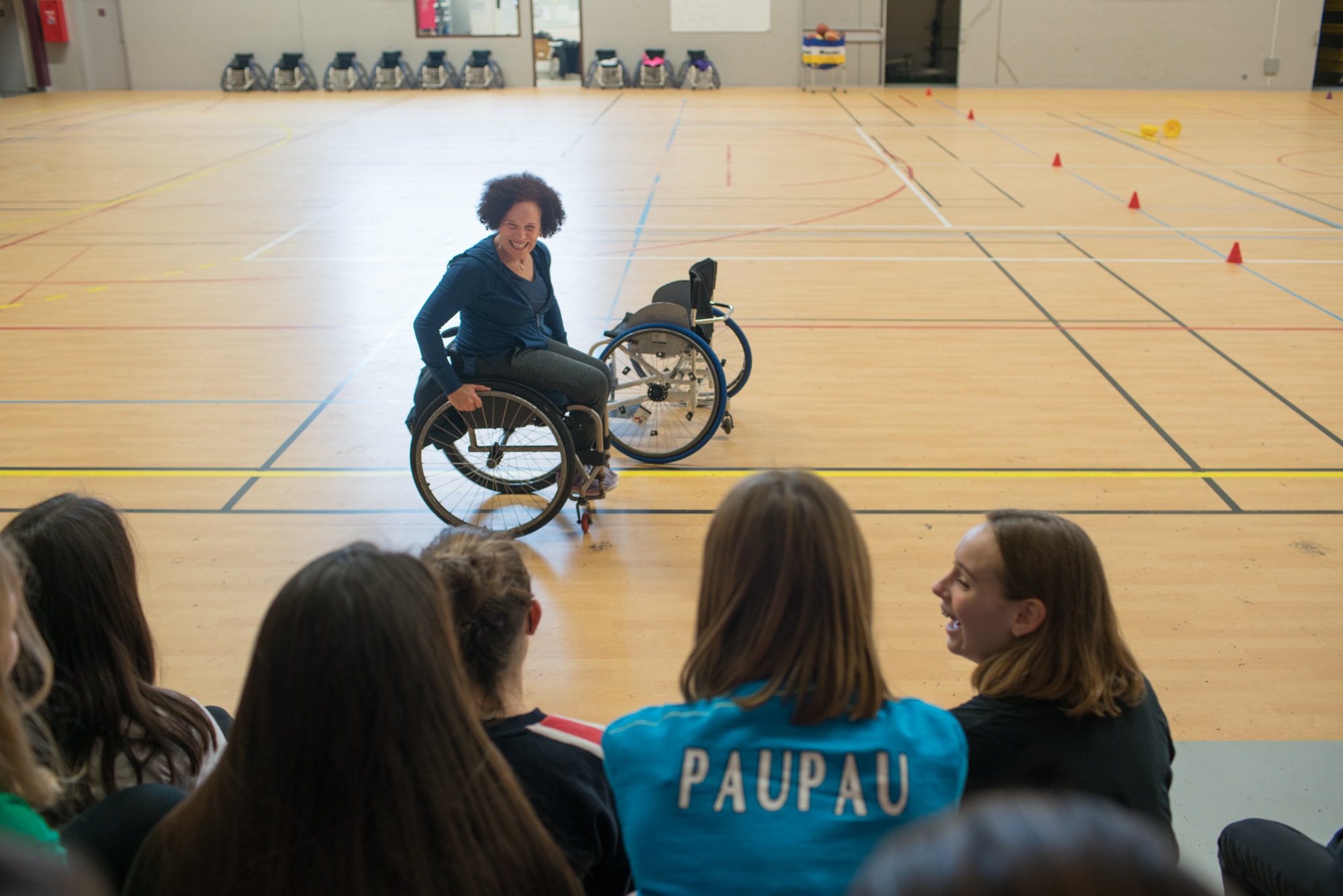 Hadda sillonne un terrain de basket avec un grand sourire en faisant face à de jeunes élèves pour les sensibiliser au handicap.