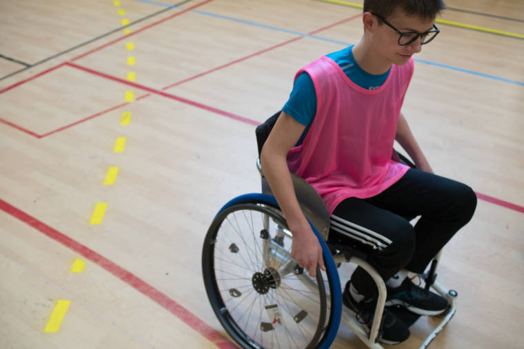 Un élève équipé d'un dossard rose sillonne le terrain de basket en fauteuil roulant.