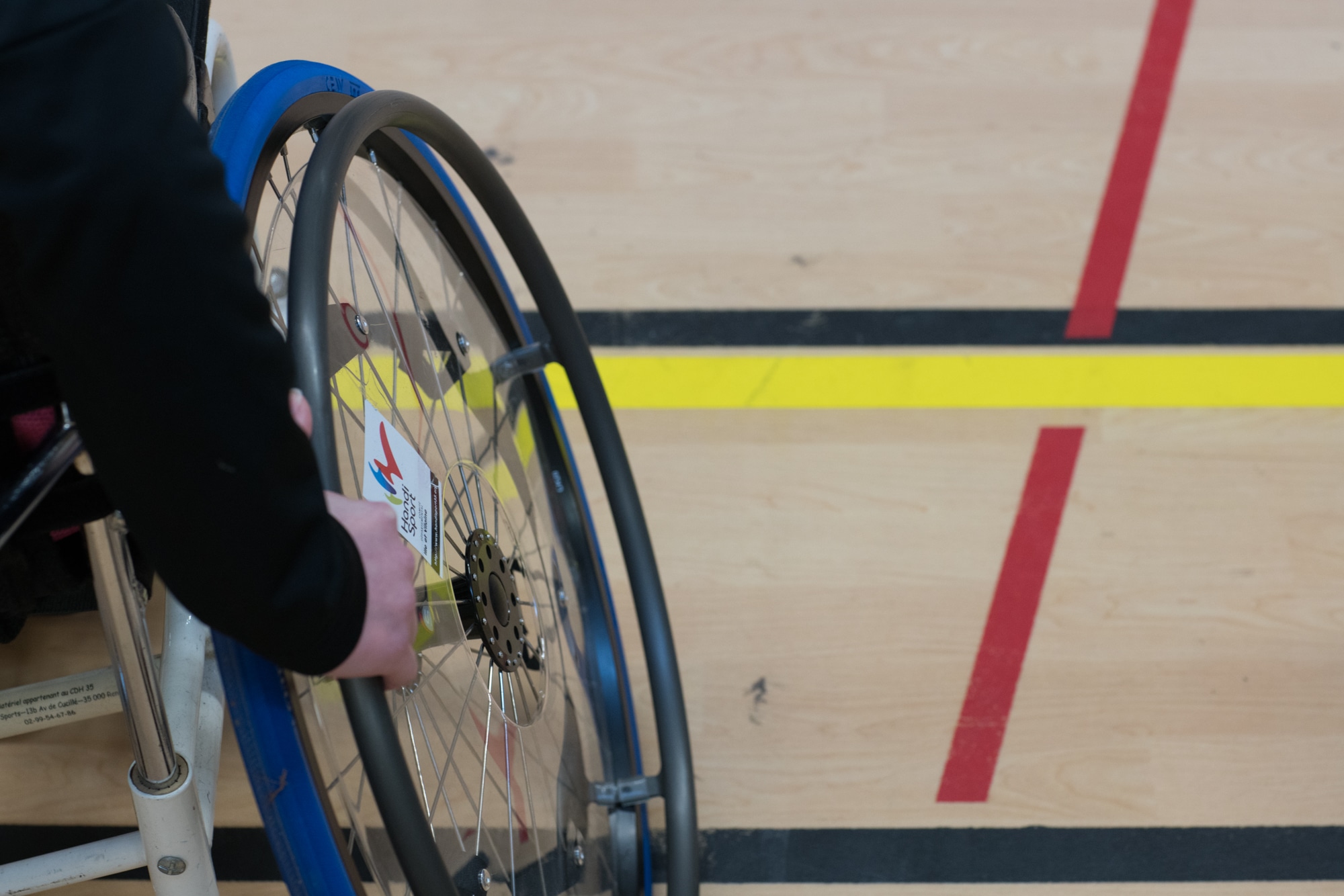 Gros plan sur une des roues d'un fauteuil roulant de sport. On peut lire l'inscription Handisport.
