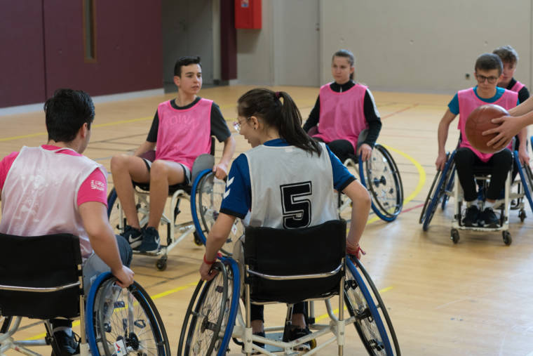Deux équipes d'élèves s'affrontent en fauteuil sur le terrain de basket.