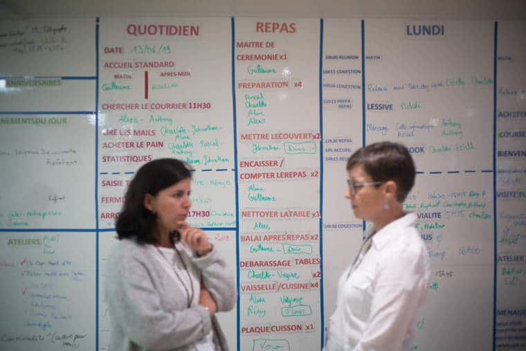 Mathilde discute avec une personnes devant le tableau des tâches.